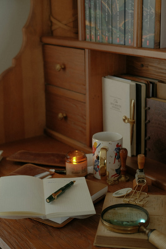 Desk with open journal, pen, candle, and magnifying glass